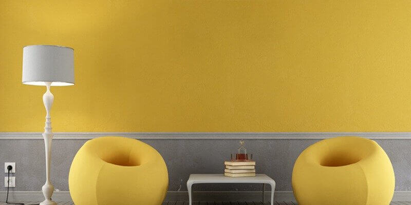 Parete giallo pantone Illuminating con poltroncine puff gialle e lampada grigia