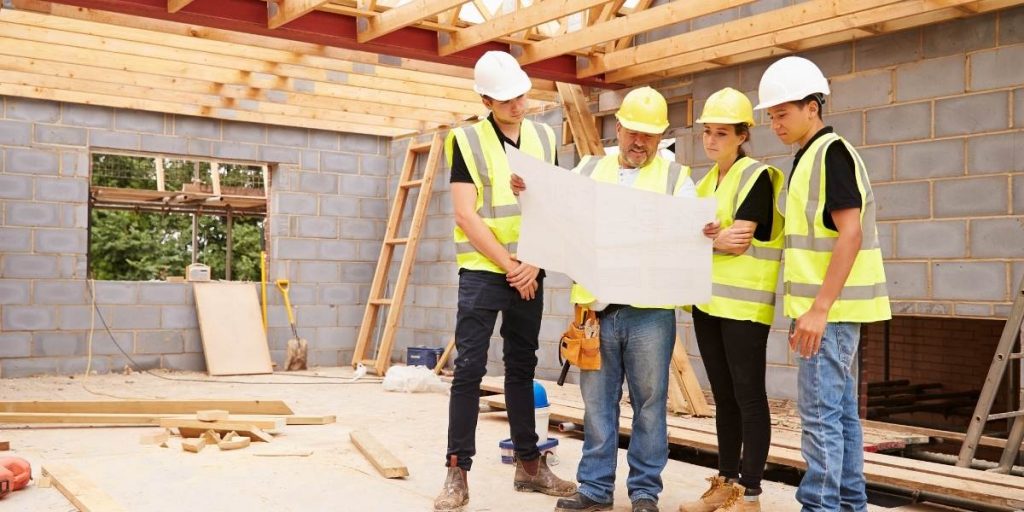 Operai con gilet e caschi di sicurezza consultano il progetto nel cantiere di una casa.