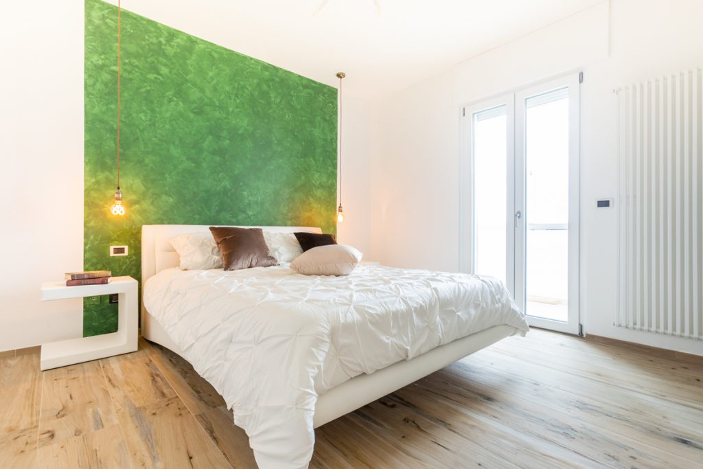 camera da letto con arredamento moderno e parete verde con effetto spugnato. Parquet di colore chiaro.