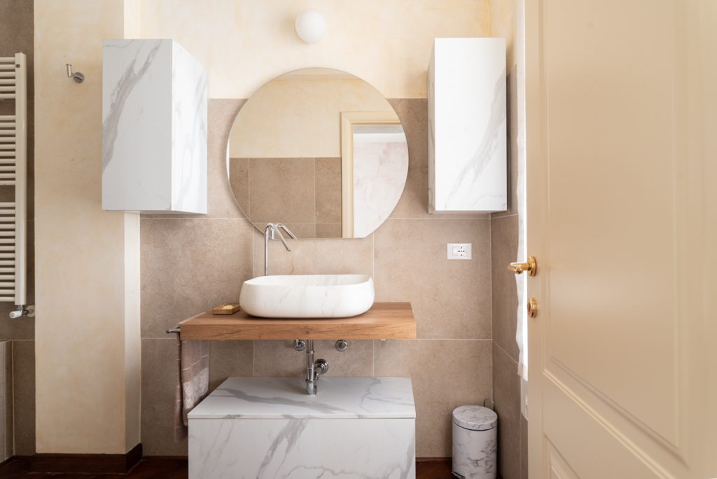 Bagno contemporaneo con sanitari e mobili bianchi effetto marmo venato ed elementi in legno chiaro