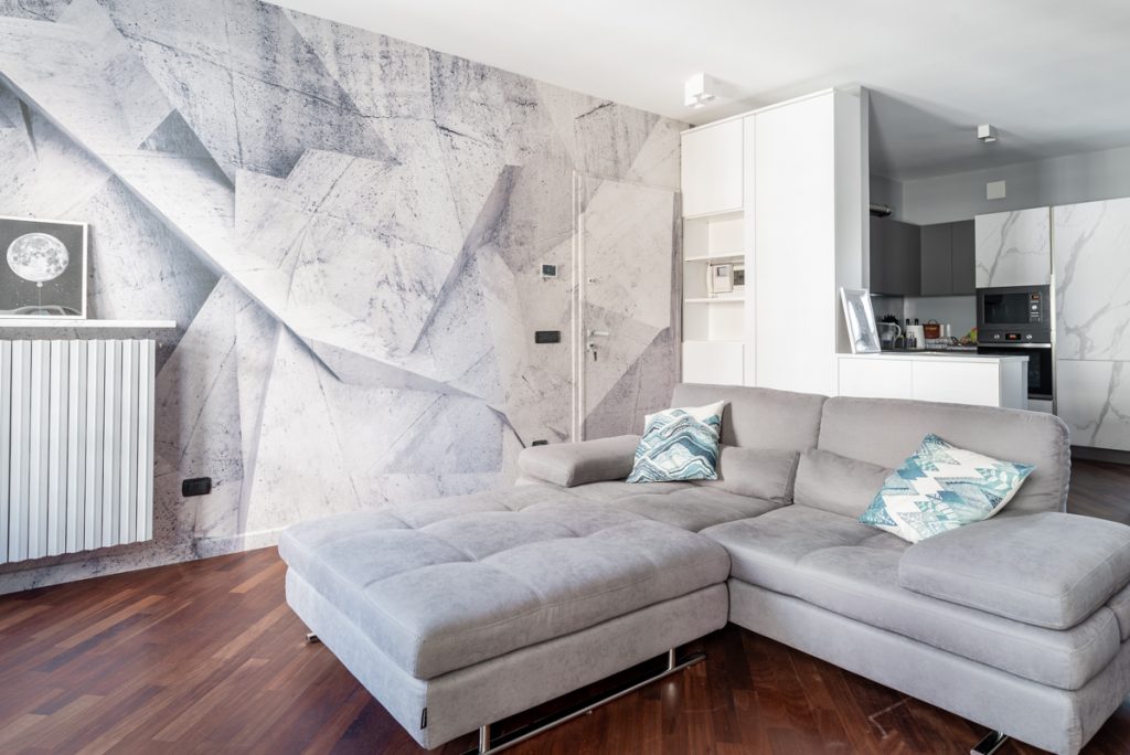 Living contemporaneo con divano spazioso grigio e carta da parati con forme geometriche