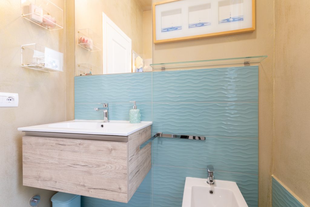 Bagno con piastrelle azzurre a con motivo onda del mare effetto tridimensionale e lavabo con mobile a sospensione