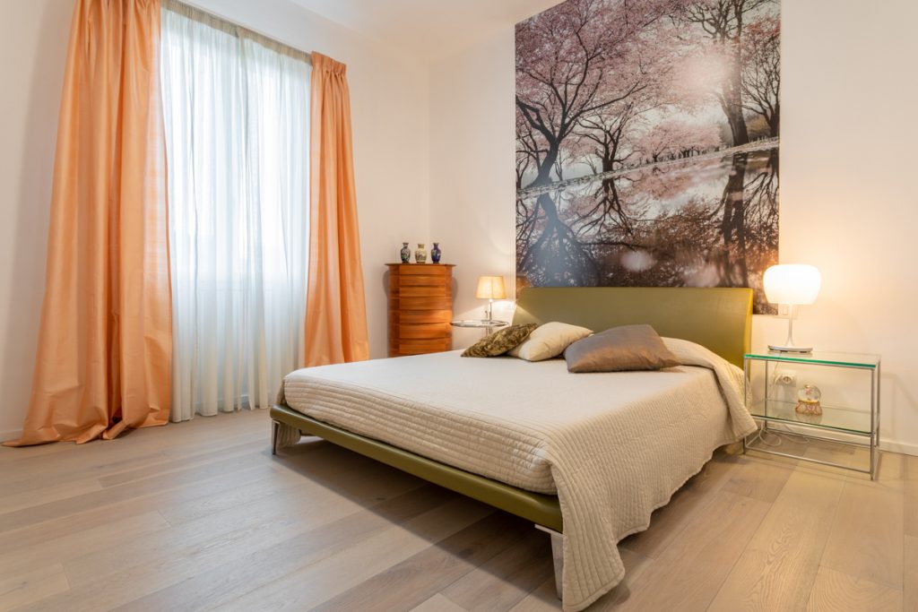 Camera da letto con arredo classico e parquet chiaro. Testata del letto con disegno di alberi.