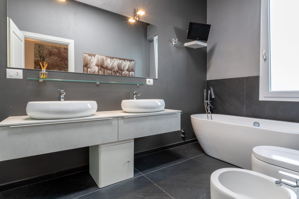 Bagno con lavabo ovale e rivestimenti in grès grigio scuro: Televisione in bagno.