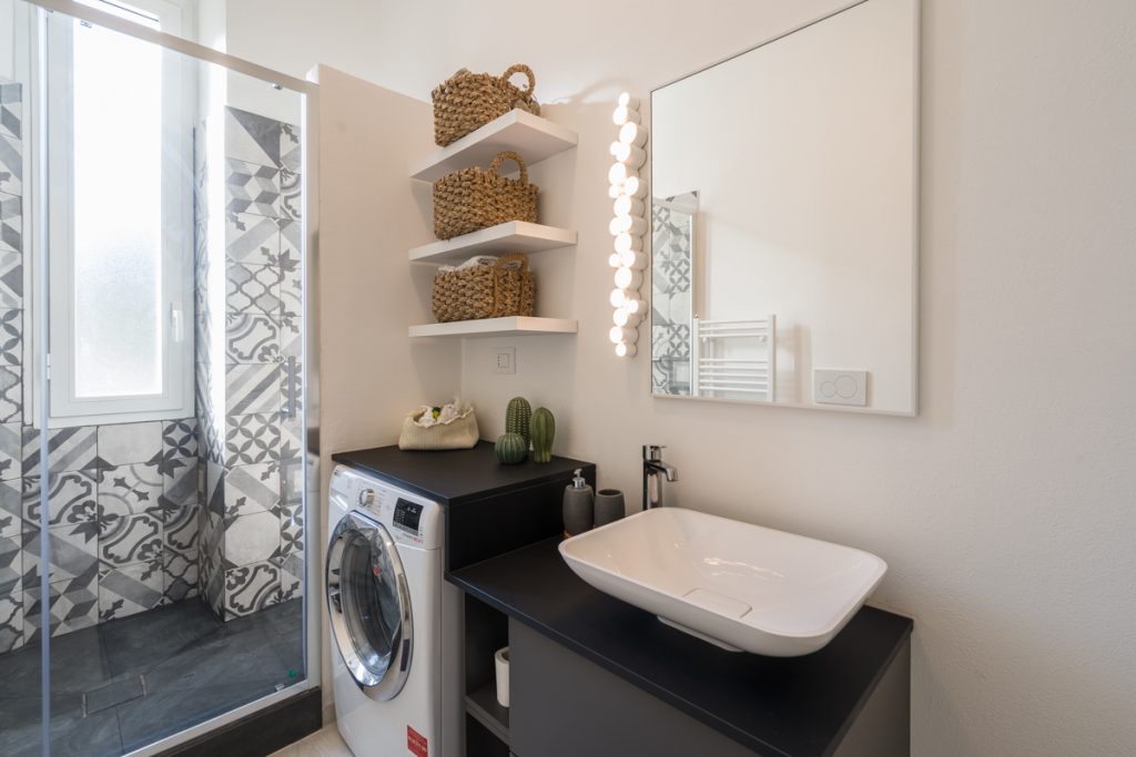 bagno moderno con lavabo d'appoggio bianco e mobile grigio scuro con accanto lavatrice.