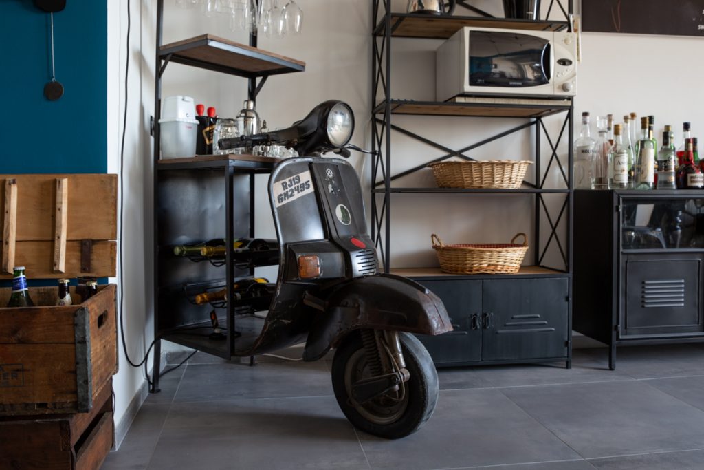 Vecchia vespa trasformata in angolo bar con accanto una libreria in legno e ferro.