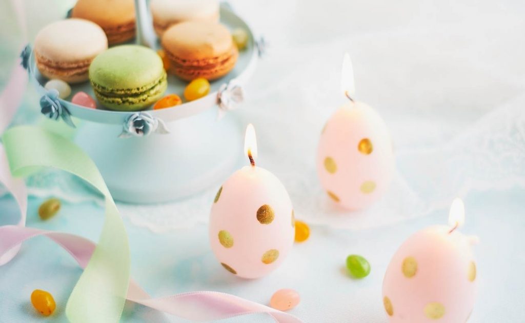 Candele per Pasqua a dorma di uovo con accanto macarons colorati.