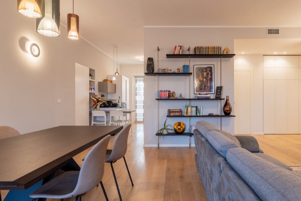 sala da pranzo con tavolo marrone e sedie grigie. Libreria a muro con libri e quadri