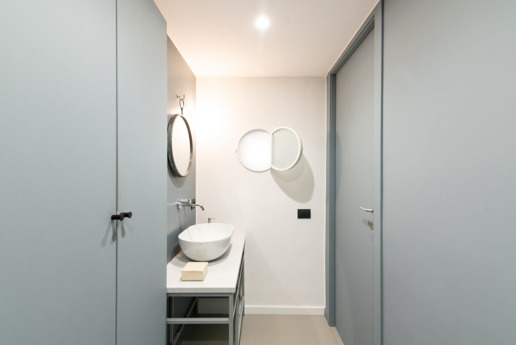 bagno moderno con lavabo d'appoggio di colore bianco e dalla forma ovale. Pareti grigie.