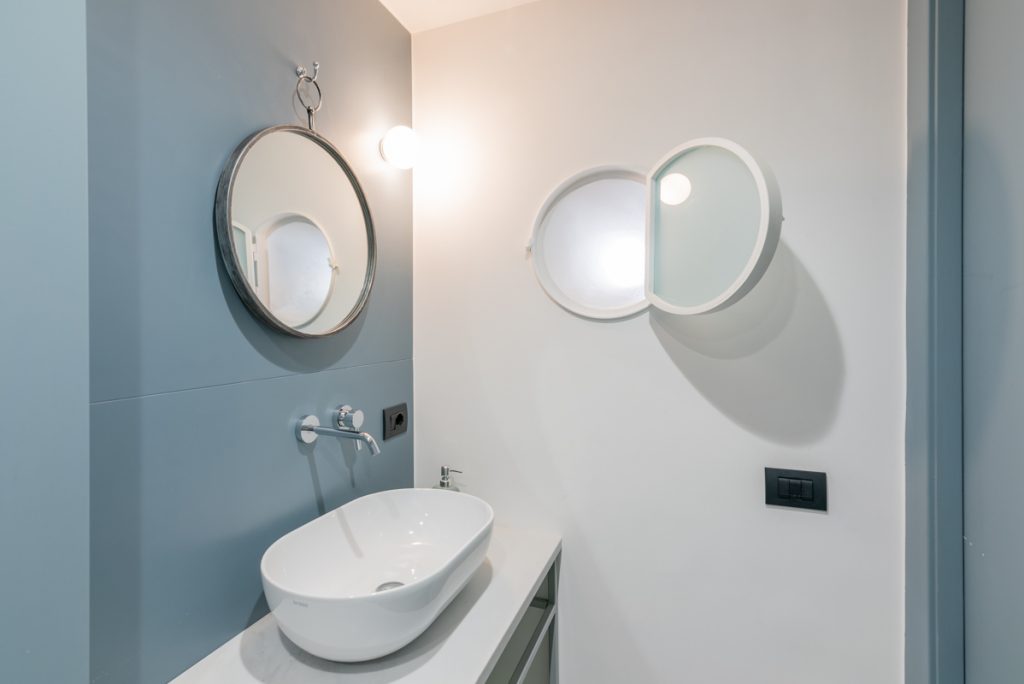 Bagno in stile moderno con lavabo d'appoggio e specchio rotondo.