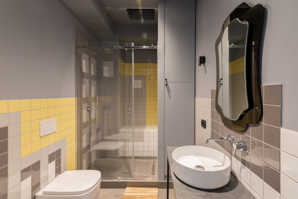 Bagno contemporaneo con sanitari bianchi moderni e piastrelle lucide di colore giallo e grigio.