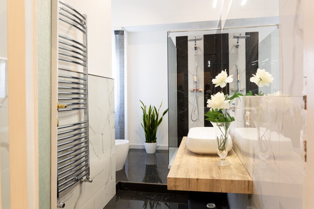 Bagno moderno con lavabo bianco d'appoggio su ripiano in legno. Rivestimenti bagno effetto marmo venato bianco e nero