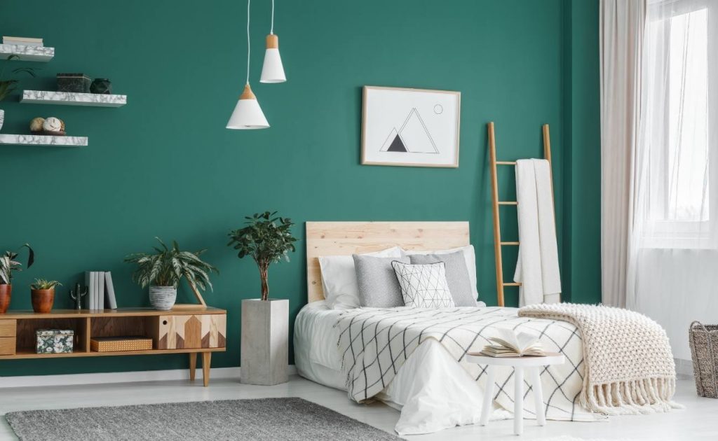 Camera da letto matrimoniale con paretei verde, mensole di marmo e lampadari a sospensione. Scala di legno appoggiata alla parete e piante verdi.