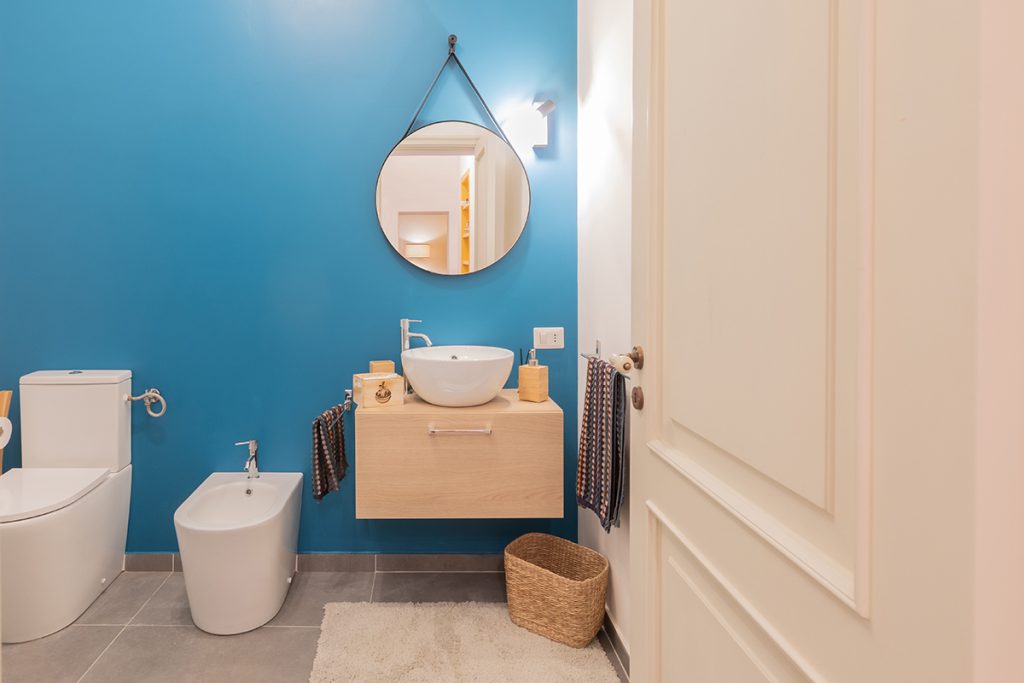 bagno moderno con lavabo bianco d'appoggio su mobile sospeso in legno. Specchio rotondo appeso alla parete del bagno.