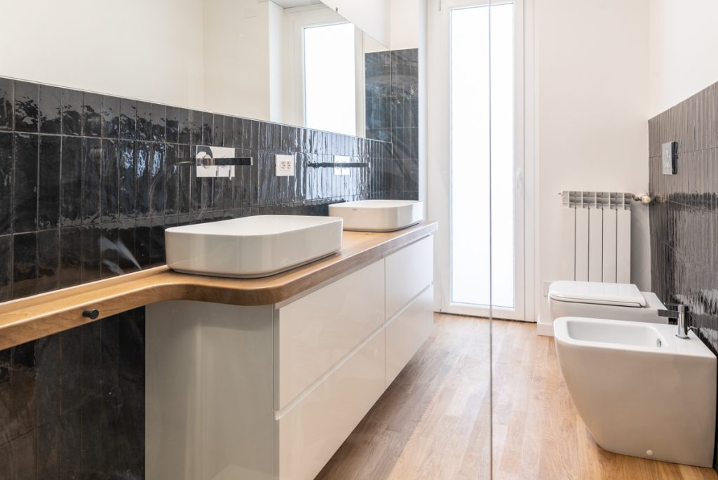 bagno moderno con doppio lavabo bianco d'appoggio e rivestimenti neri.