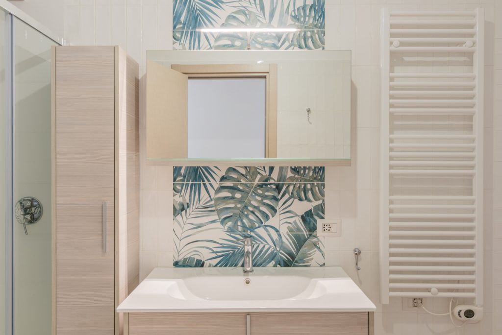 bagno moderno con lavabo bianco a sospensione e piastrelle con fantasia floreale.