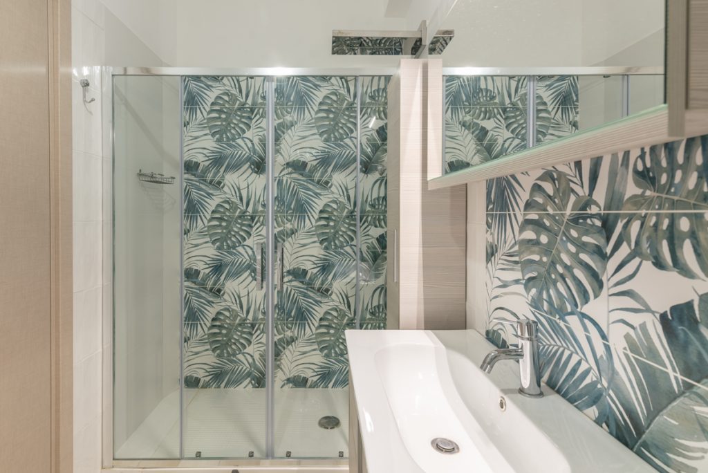 Bagno con rivestimenti in gres porcellanato con foglie di monstera.