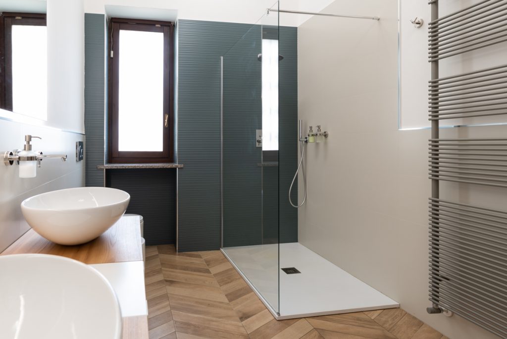 Bagno con box doccia vetrato e rivestimenti grigi.