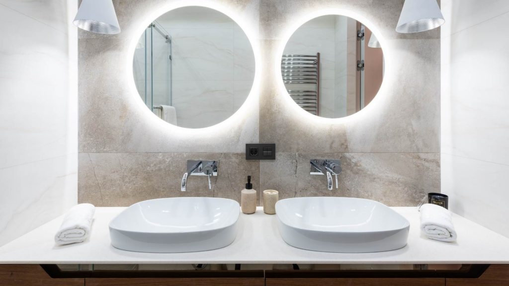 Bagno con doppio lavabo bianco e due specchi rotondi.