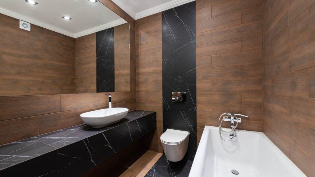 bagno con rivestimenti in marmo nero e legno con lavandino da appoggio bianco dalla forma ovale.