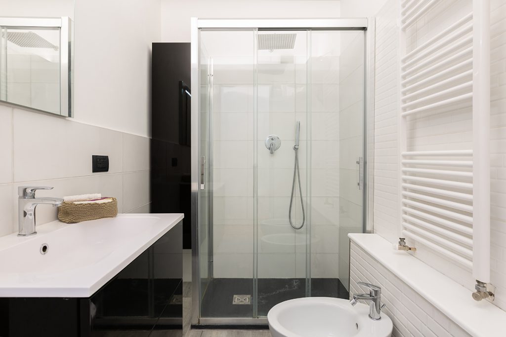 Bagno moderno con box doccia vetrato e rivestimenti bianchi.