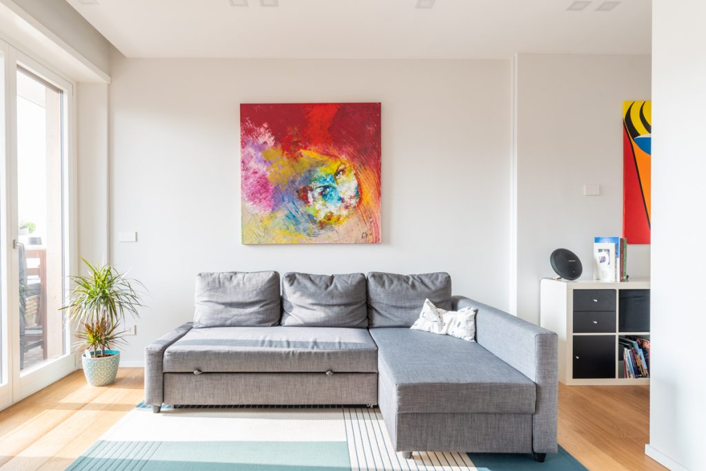 ristrutturazione casa torino soggiorno moderno con divano angolare grigio e quadro colorato su parete bianca.