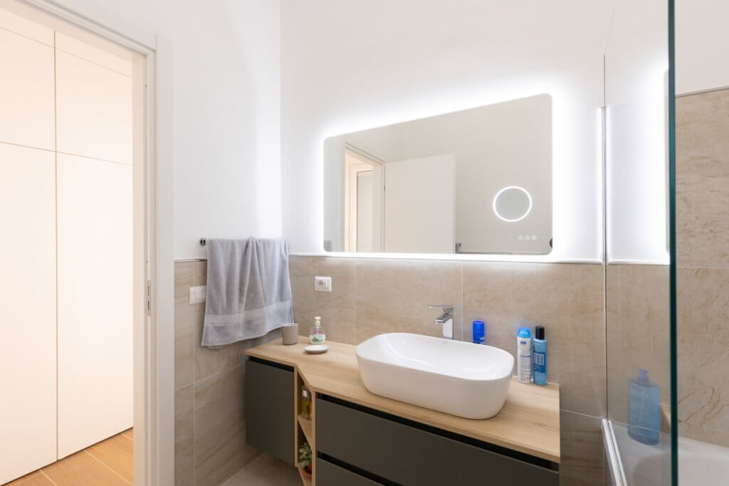 Bagno con spacchio rettangolare con luci a led e lavandino bianco d'appoggio su mobile in legno.