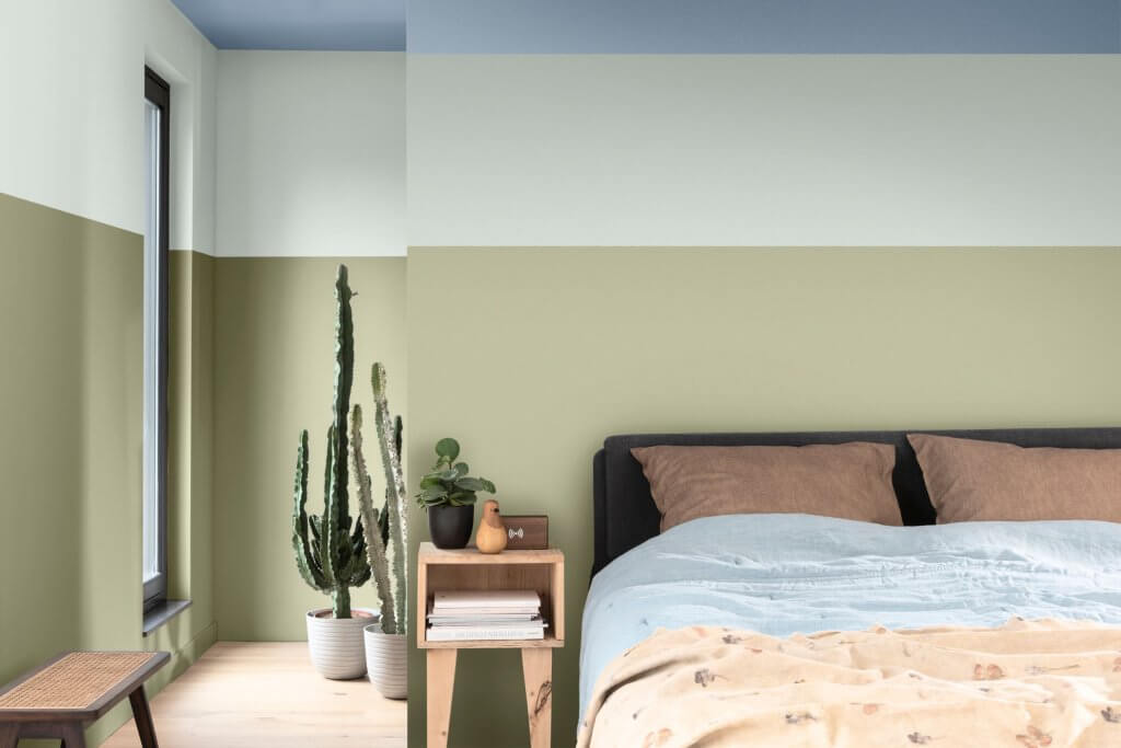 Colore pareti, interni casa. Camera da letto con parete a righe di colore verde con cuscini marroni e cactus laterali