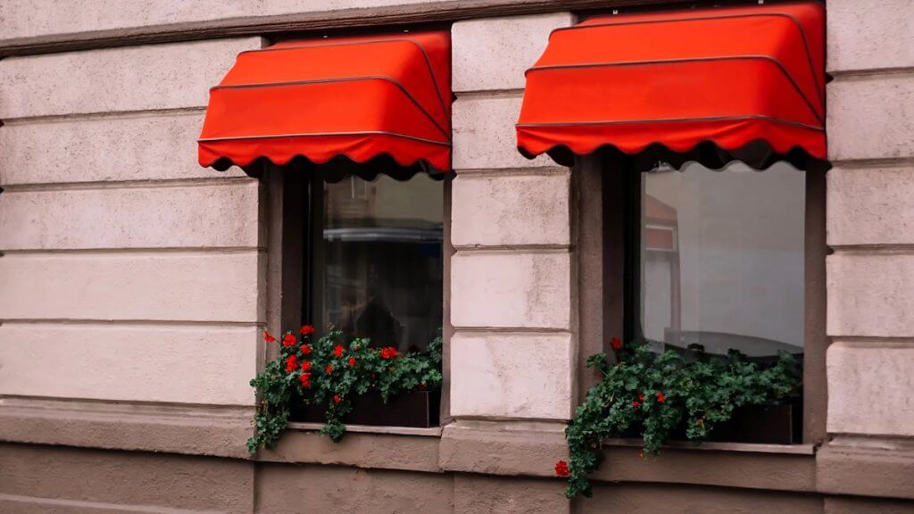 Tende da sole a cappottina di colore rosso con vasi e piante