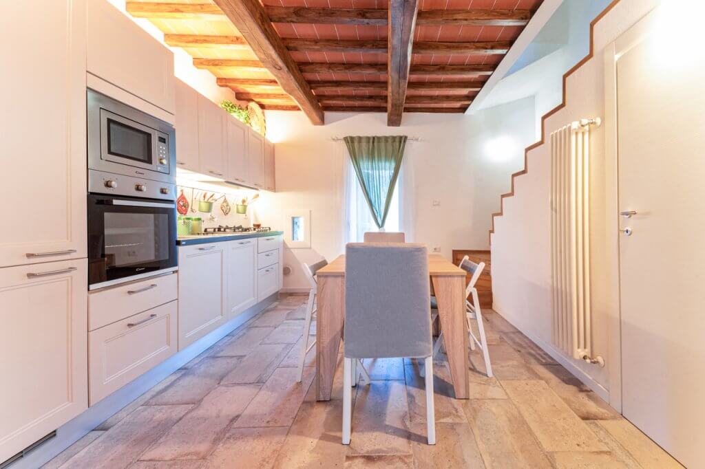 Cucina con rivestimenti in legno bianco, pavimento in gres e scala laterale