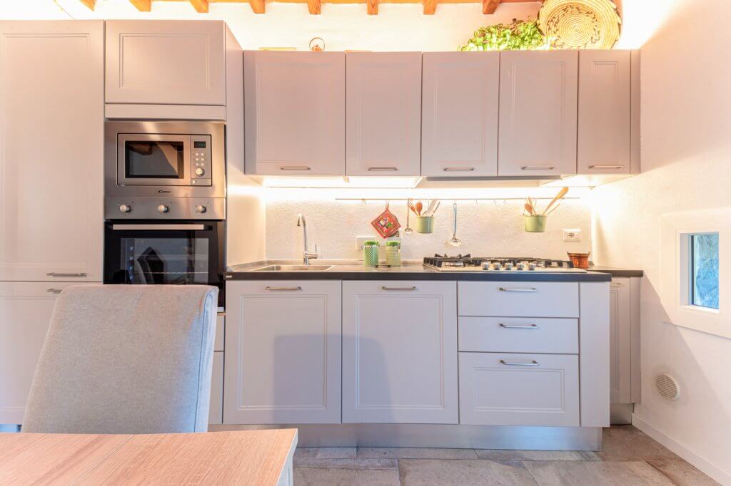 Cucina con illuminazione, rivestimenti in legno bianco, piano cottura nera e forno laterale