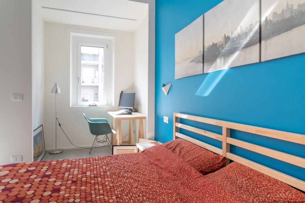 Camera da letto con lenzuola colorate, parete azzurra e bianca con tavolo in legno