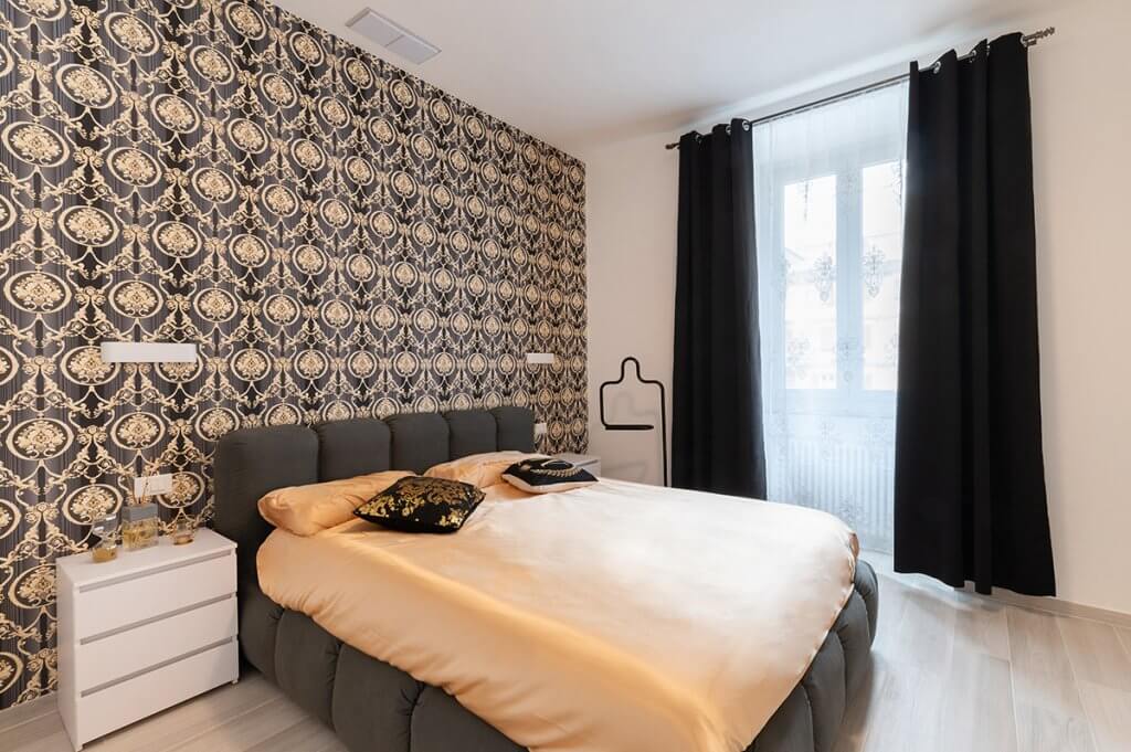 Camera con letto con boiserie, carta da parati dallo stile barocco, parquet in legno chiaro e finestra laterale