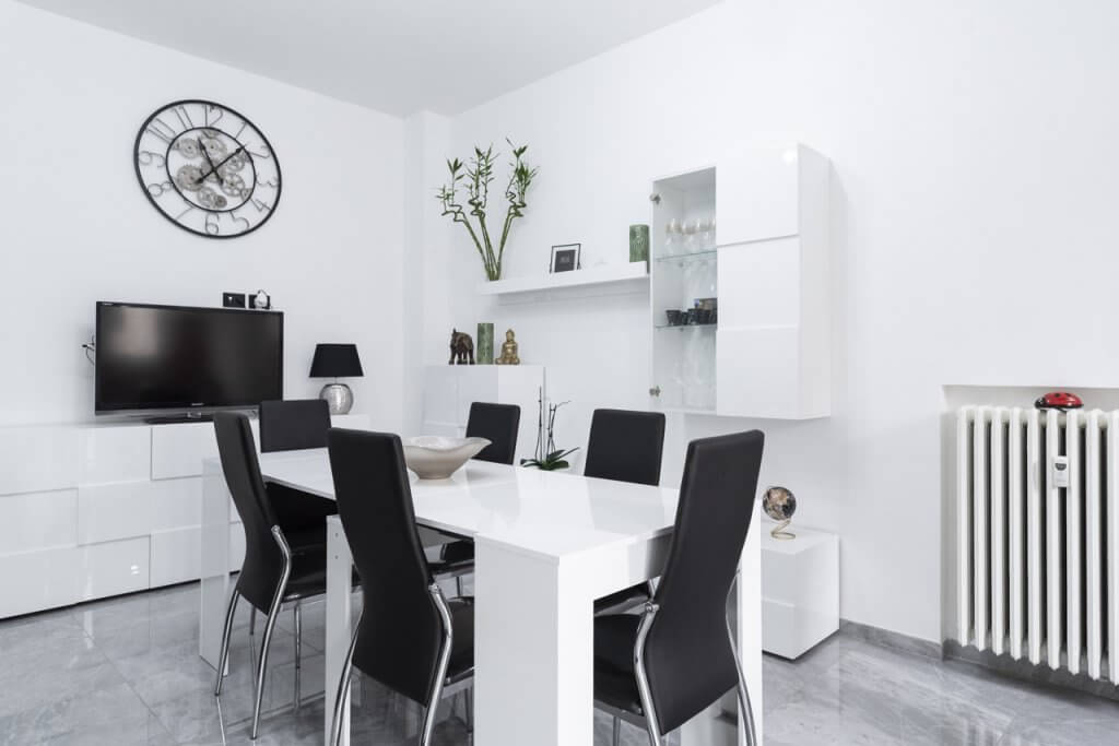 Zona pranzo con tavolo bianco, sedie, mobili dal design moderno e libreria con vetro